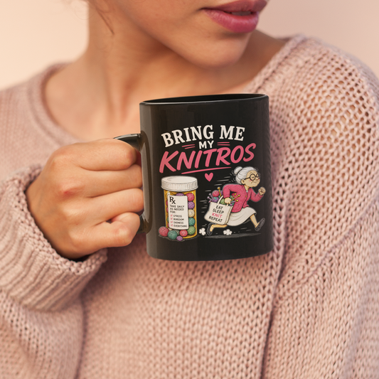 A woman in a pink knit sweater holds a black ceramic mug with the text 'BRING ME MY KNITROS' and a small illustration of knitting figures.