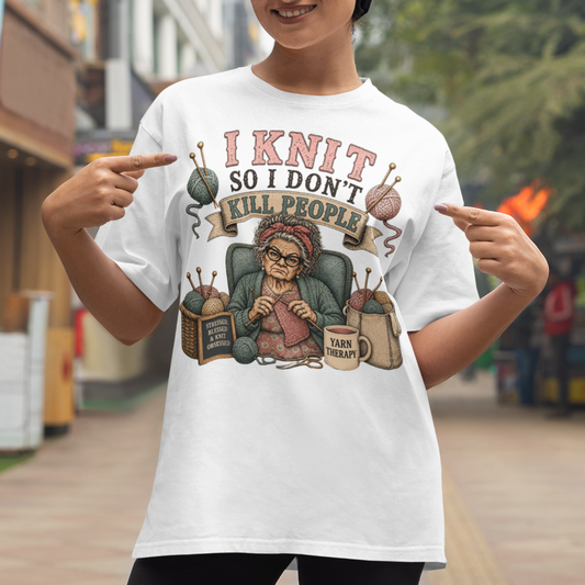 Person wearing a white t-shirt with a graphic and text 'I Knit So I Don't Kill People' pointing at it.